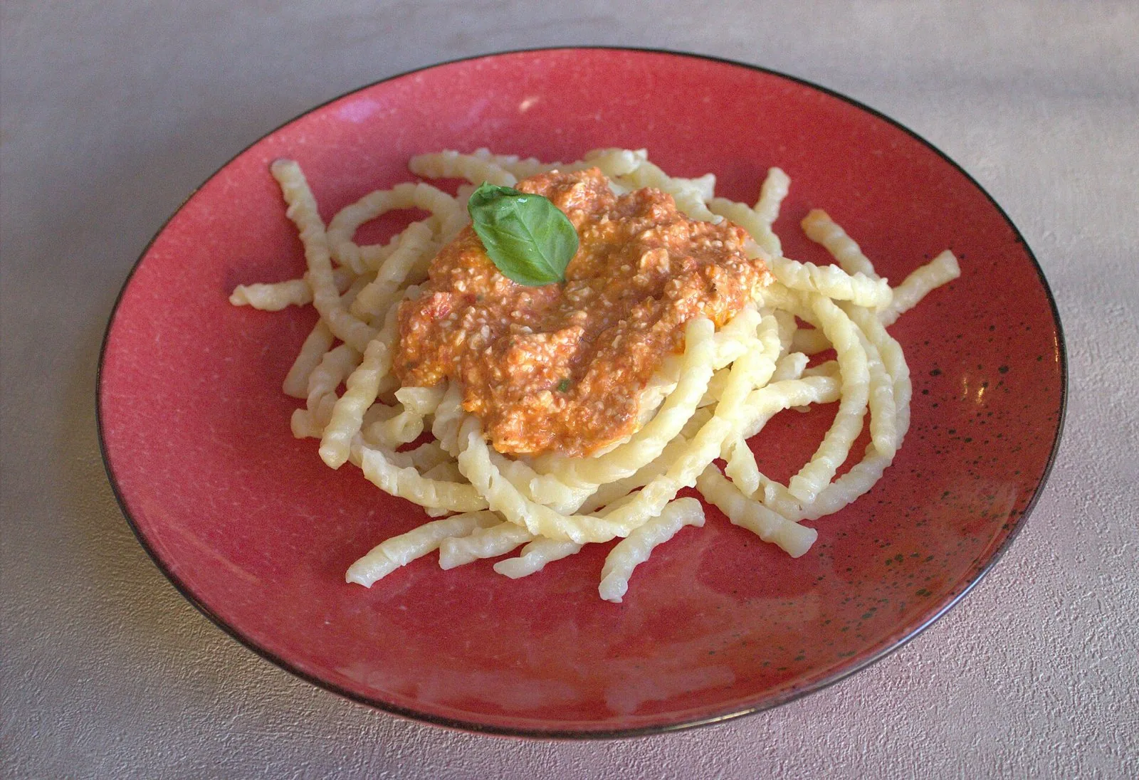 Busiate al pesto alla trapanese servite in un piatto rosso